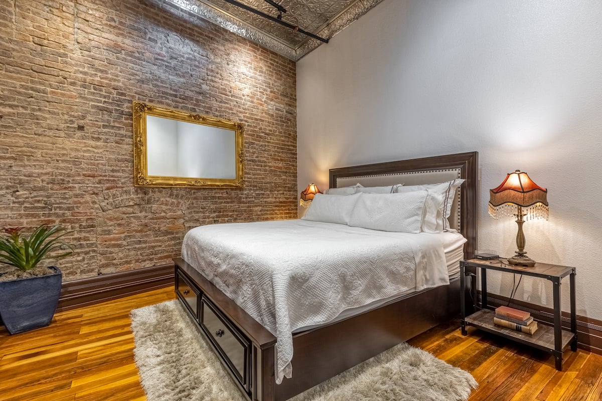 King bed against an original brick wall with gold mirror